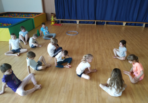 Dzieci siedzą na podłodze i wykonują ćwiczenia rozciągające.